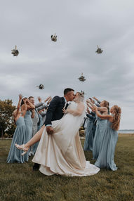 Bride and groom kiss as wedding party tosses bouquets into the air at a Mackinac Island wedding.