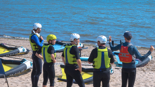 Des personnes écoutent un briefing debout au bord de l'eau avant d'aller faire du wingfoil à Séné