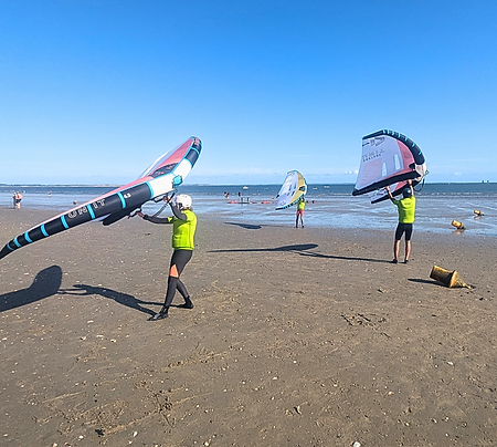 Des personnes qui tiennent une voile dans leur main sur la plage pendant un cours de wingfoil avec Wing Latitude à Damgan