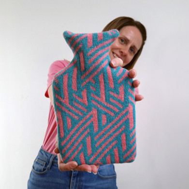 Woman holding a small knitted hot water bottle cover in green and pink