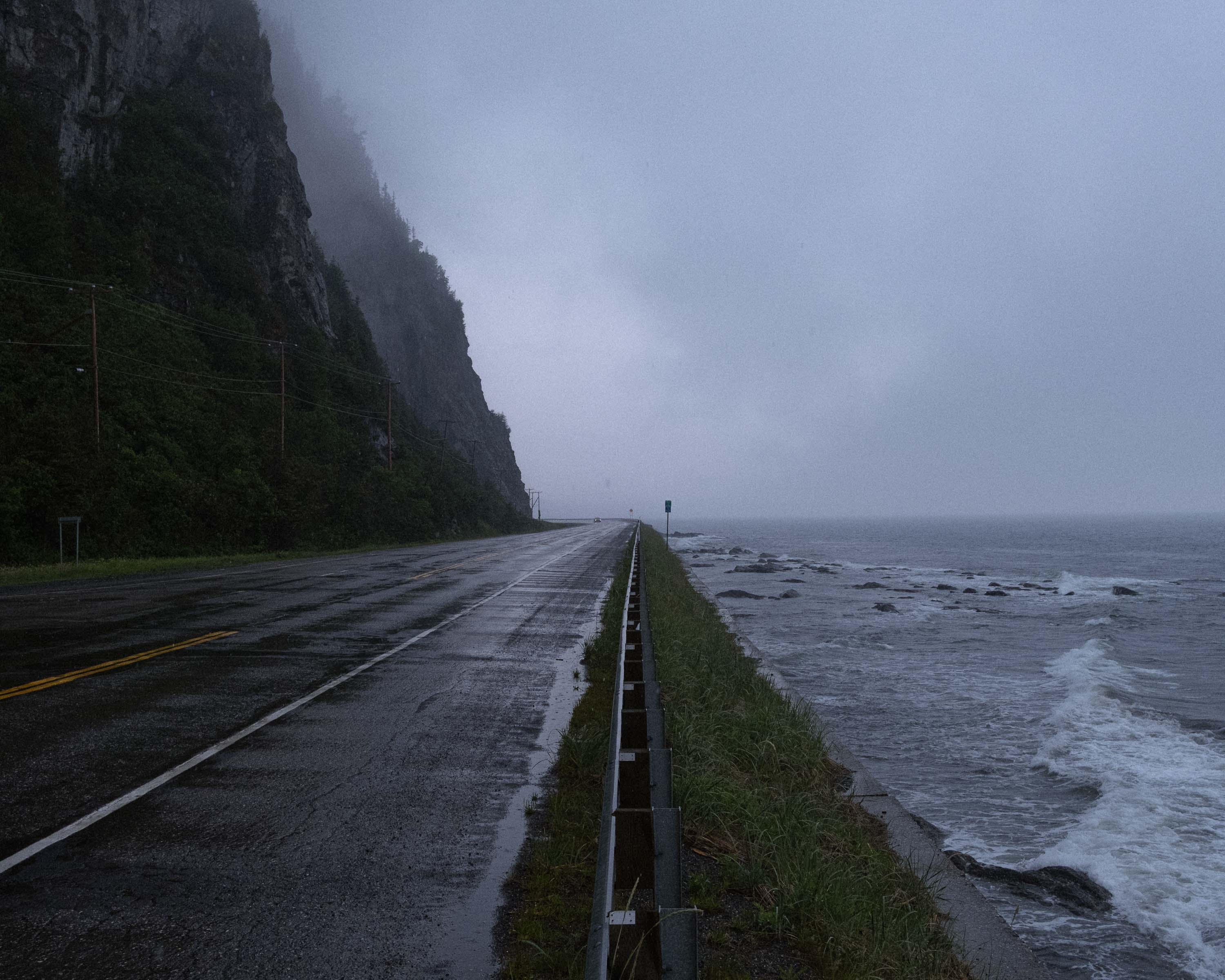 Route côtière mouillée longeant une falaise sous la brume.