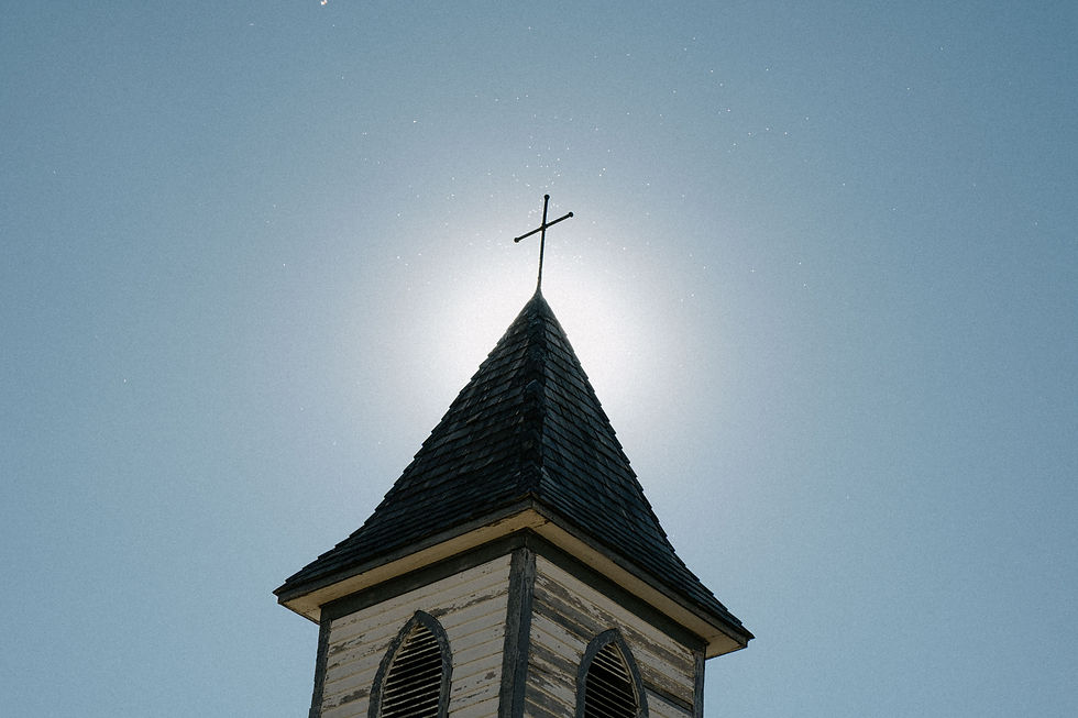 Wooden church steeple with cross under a sunny sky.