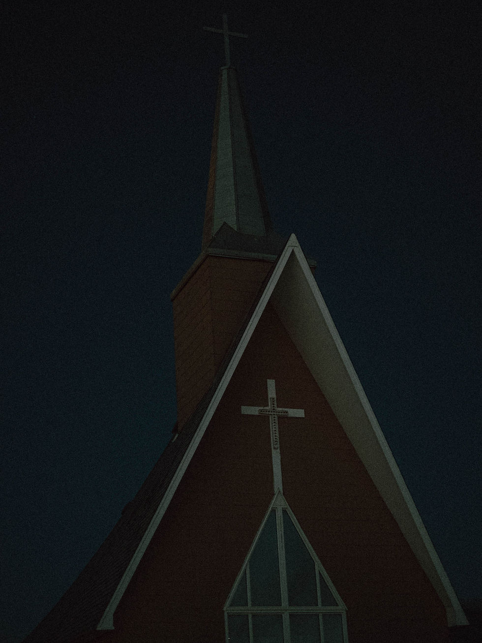 Pointed church steeple with a cross under a dark sky