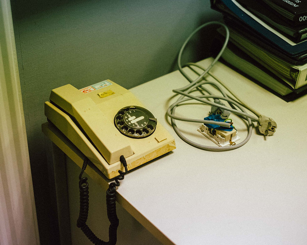 An old beige rotary phone sitting on a white desk.