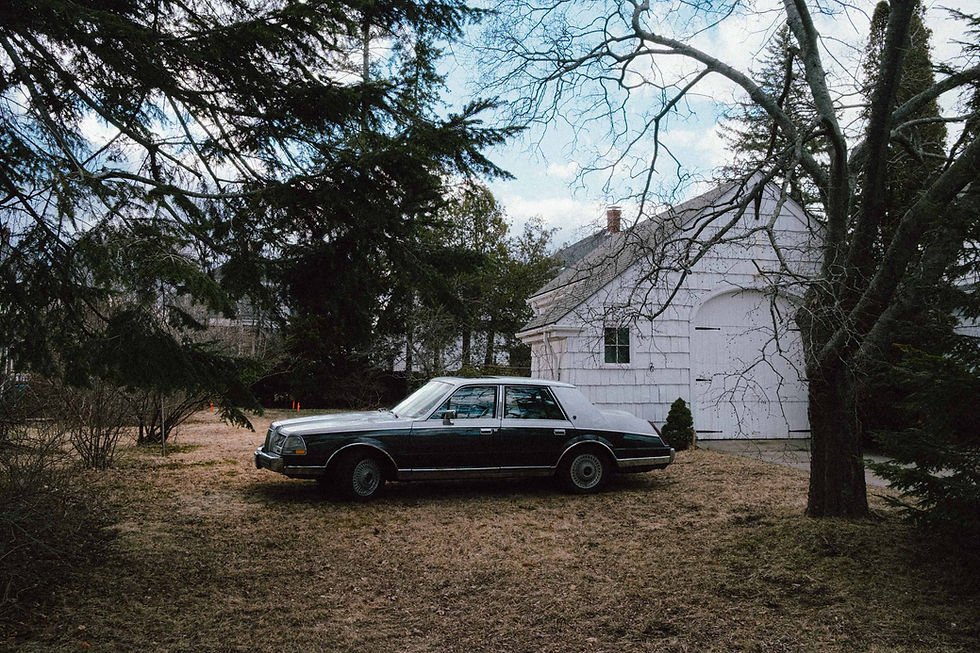 Vintage sedan parked in front of a white garage surrounded by trees.