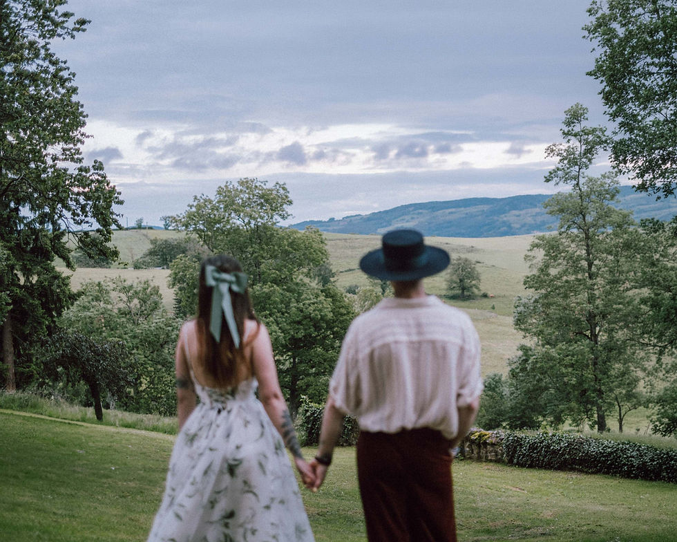Married couple seen from behind, holding hands, facing a landscape.