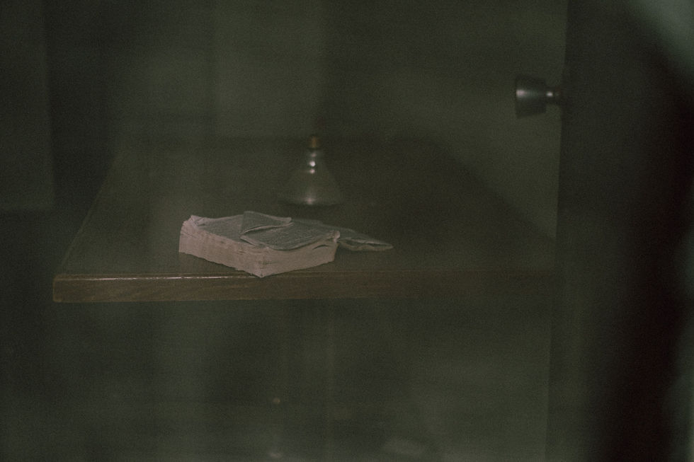 An old bible and a candlestick on a dark wooden table through a window.