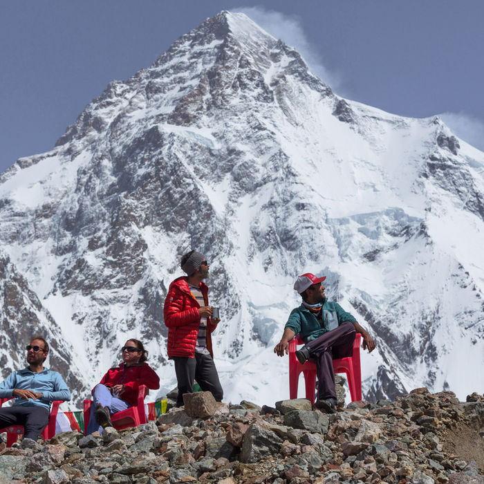 Group of climbers approach the base of a massive snow-covered pyramid-shaped mountain peak under blue skies, with their small figures emphasising the scale of the mountain.