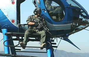 Armed male sitting on the open door of a stationary helicopter