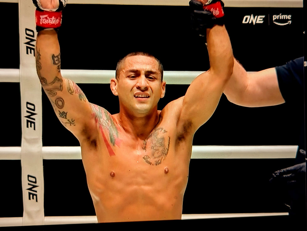 Gilbert Nakatani raises arms in victory in a ring, wearing red gloves. "ONE" branding visible. Confident expression.