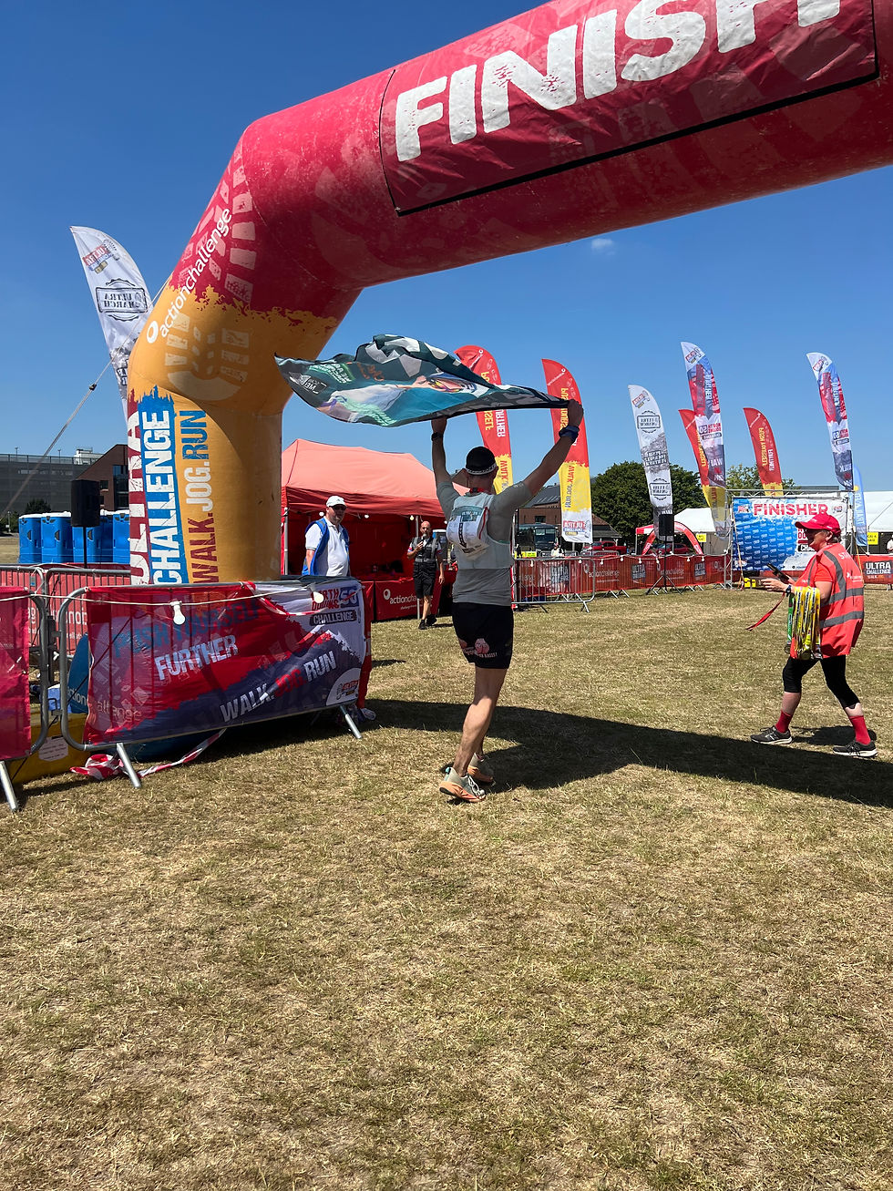 Runner crosses finish arch at outdoor race, holding a flag as volunteers stand by under a clear blue sky.