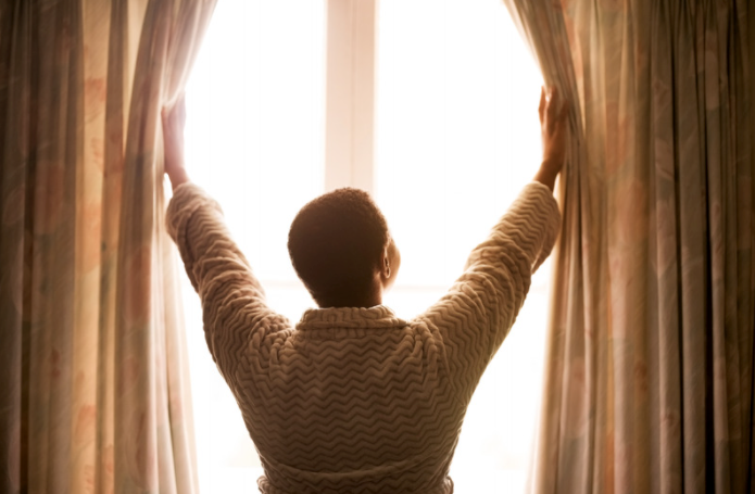 Black woman opening curtain blinds to see the morning sunrise