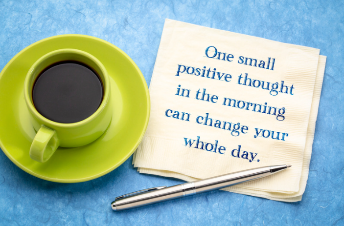 Green coffee cup with stainless steel pin on table with a positive quote written on a napkin