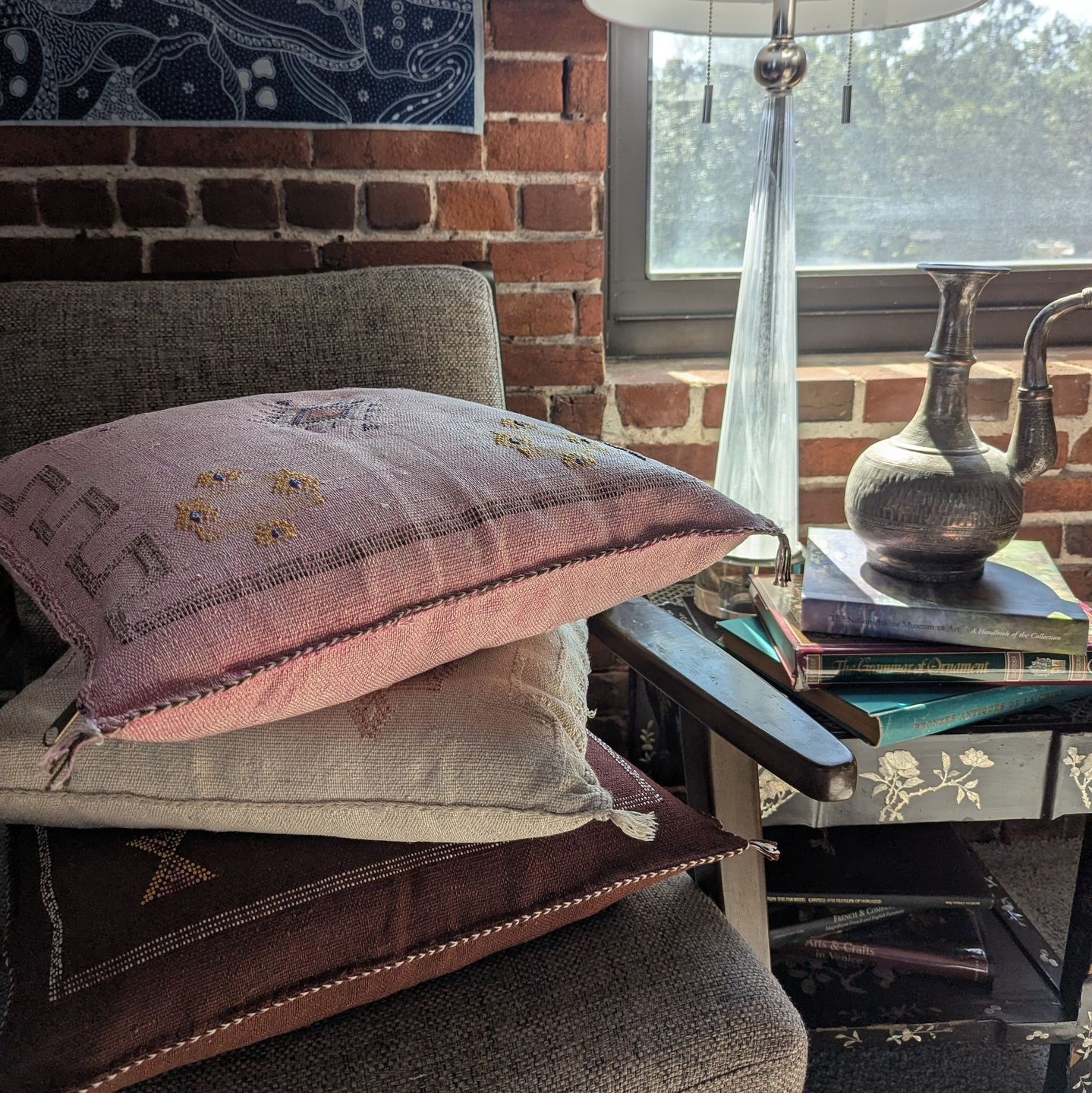 Nadia Moroccan cactus silk throw pillow in deep red with geometric embroidery, stacked beneath pink and white cushions on a c