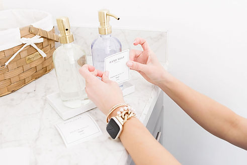 Hands placing "HAND SOAP" label on clear dispenser near "LOTION" on marble. Bathroom organization in Lexington, KY by Tara M Stewart team