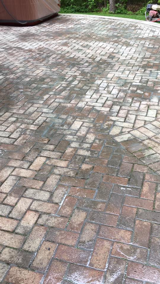 Wet brick patio or driveway with a curved edge, green lawn beyond, and a covered object at the top left after rain