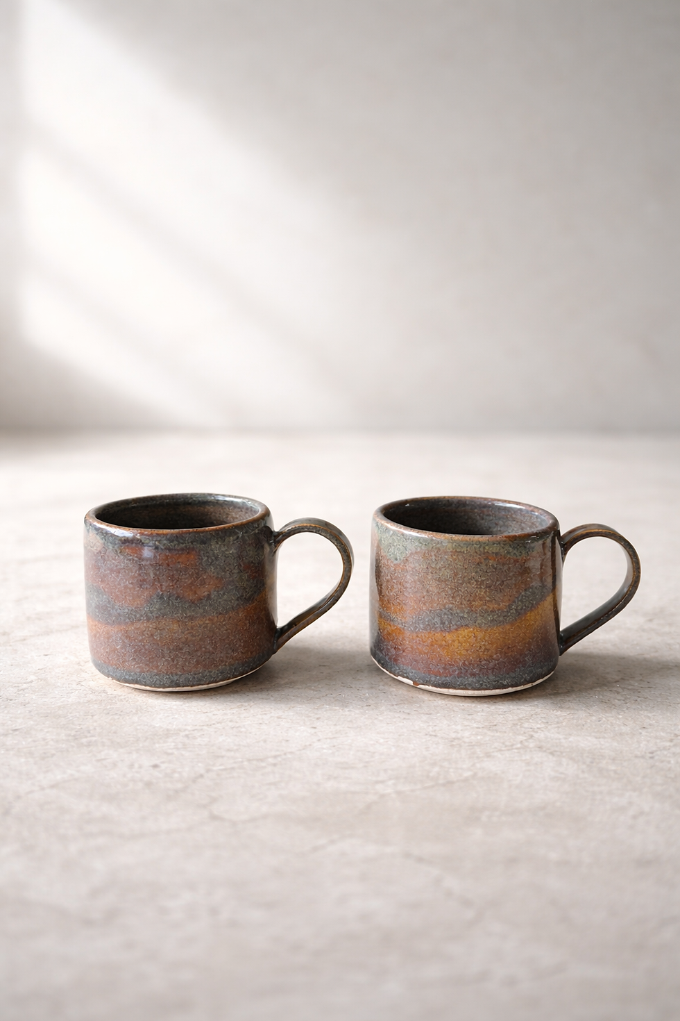 Solstice handmade espresso cup pair side by side on white surface and natural clay edge with handle