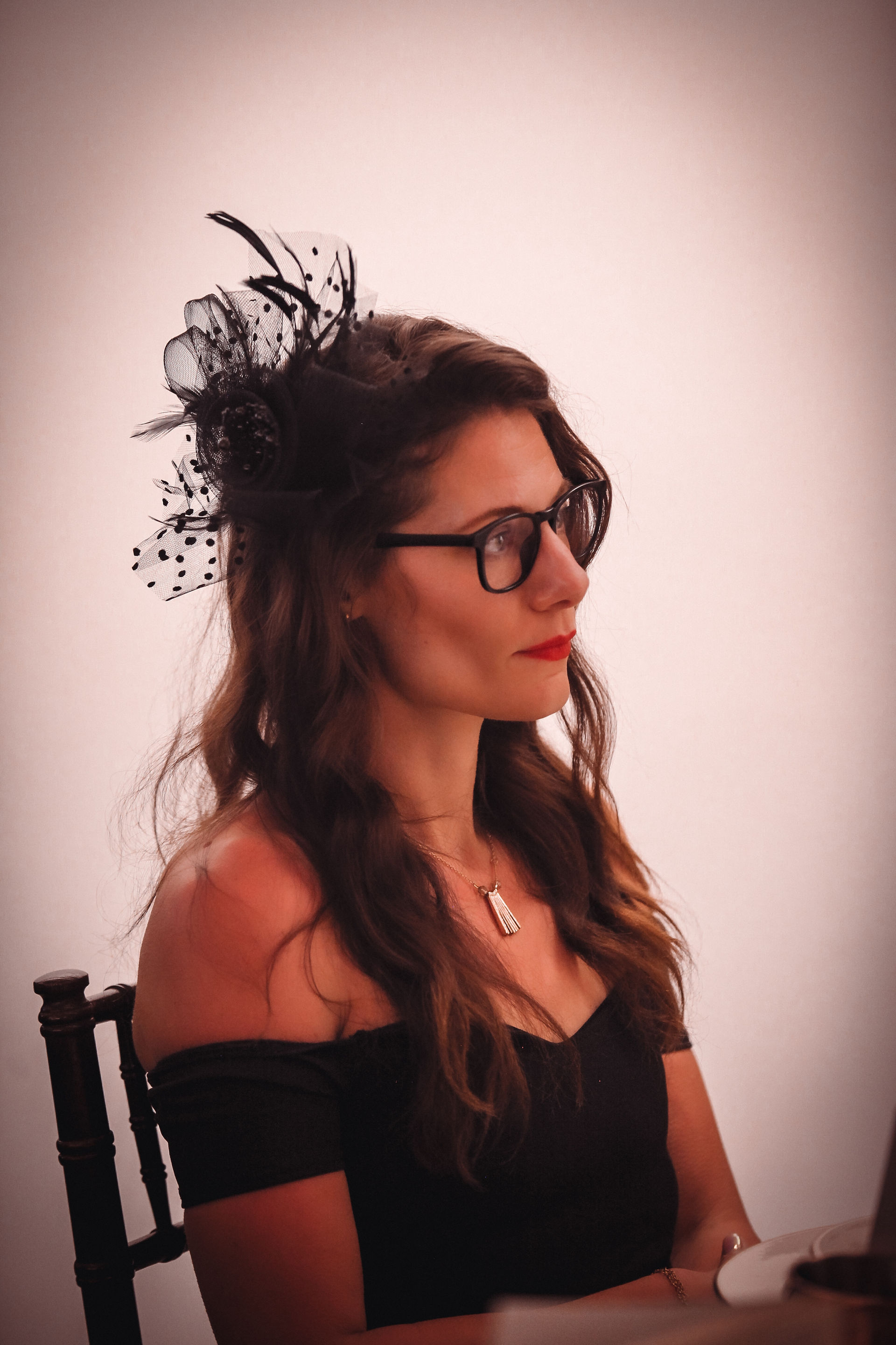 Woman with dark hair and glasses, black feathered hat
