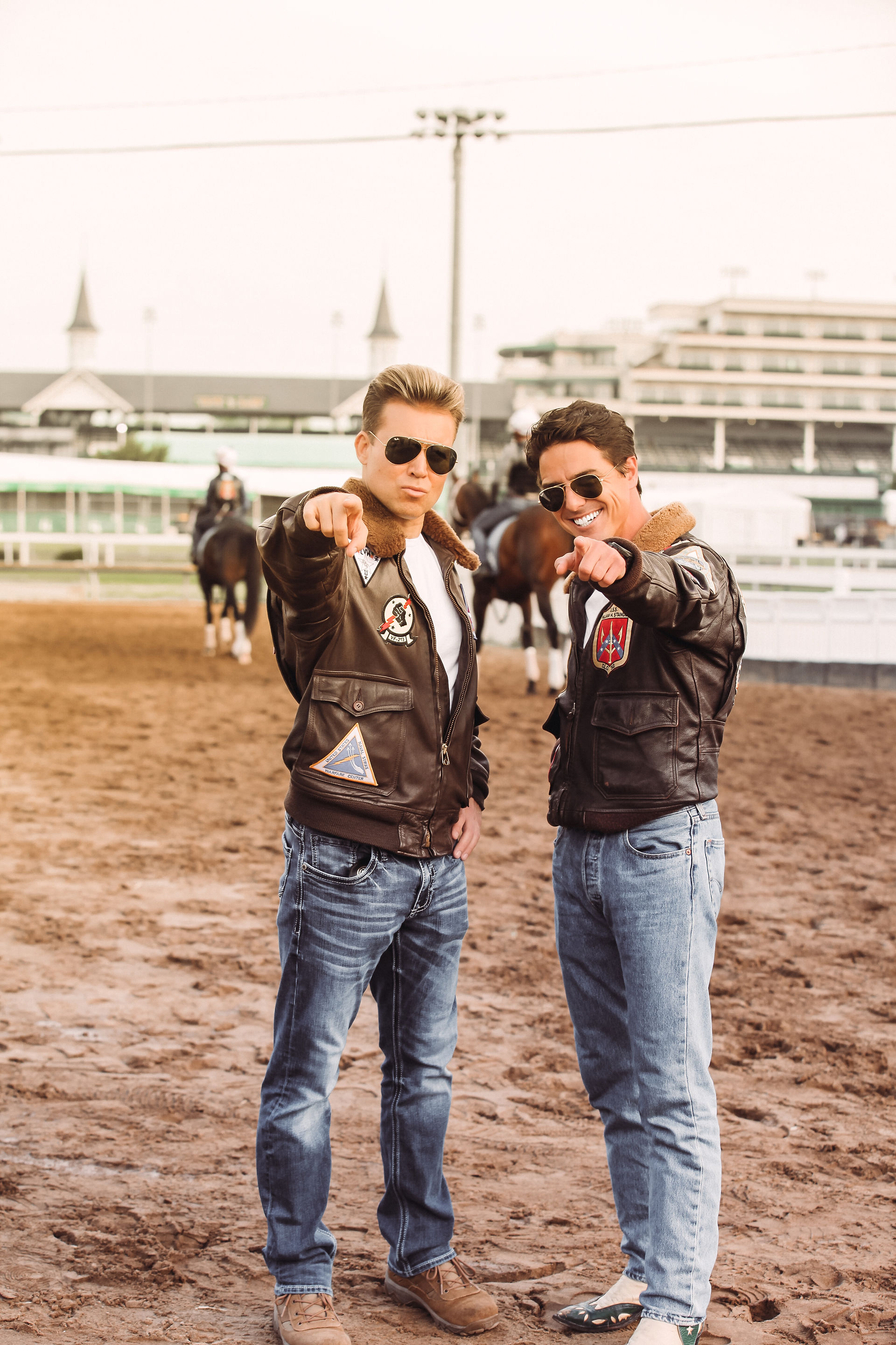 Two men in bomber jackets at the Kentucky Derby point playfully at the viewer.