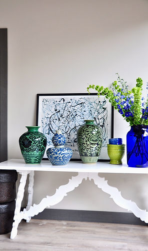 A sideboard styled with hand-painted celadon pots from Thailand, vintage glass vases filled with Bells Of Ireland sprigs and a framed Jackson Pollock print.