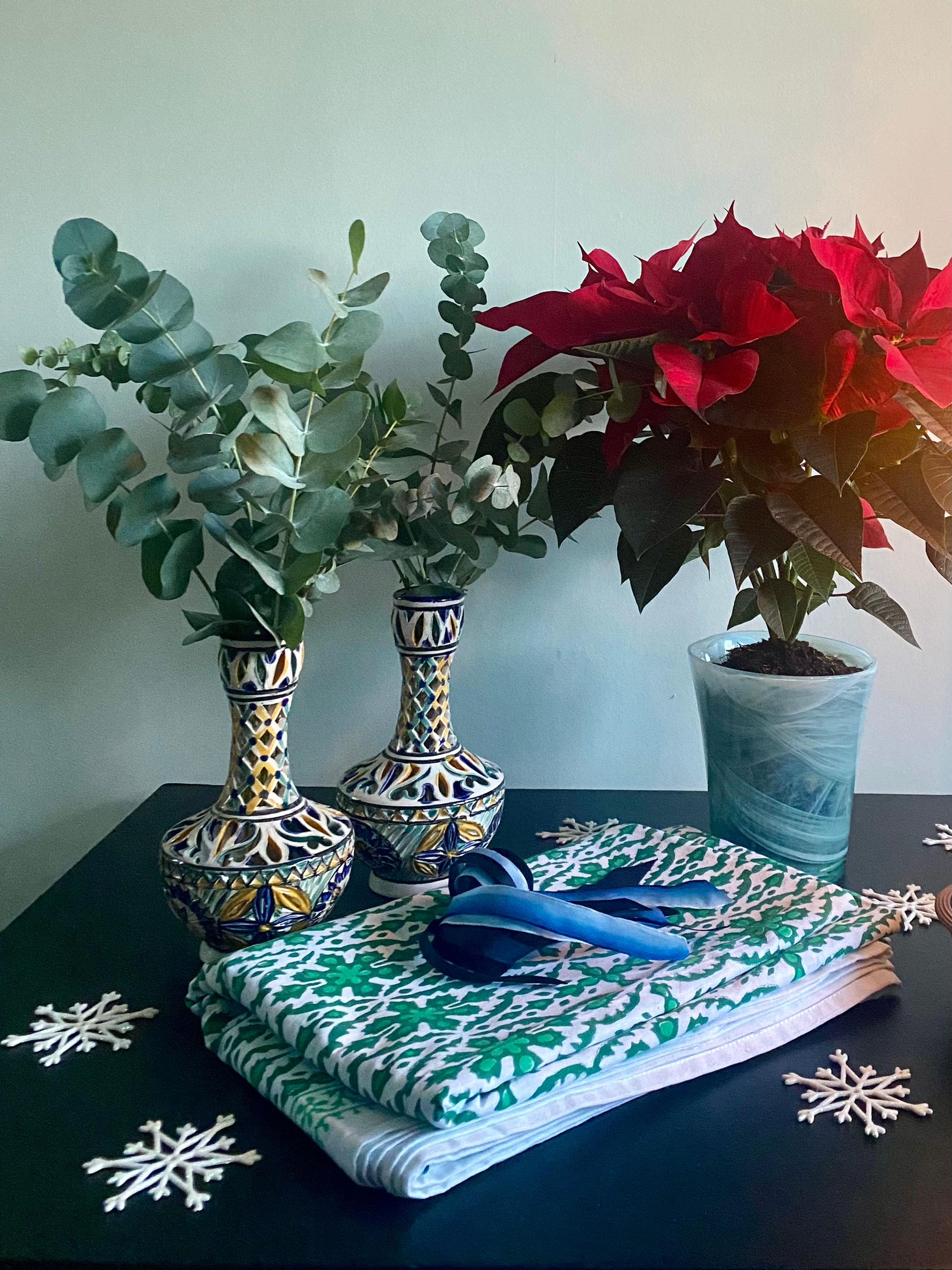 A Christmas table setting with red potted Poinsettia and hand-painted vases filled with eucalyptus.