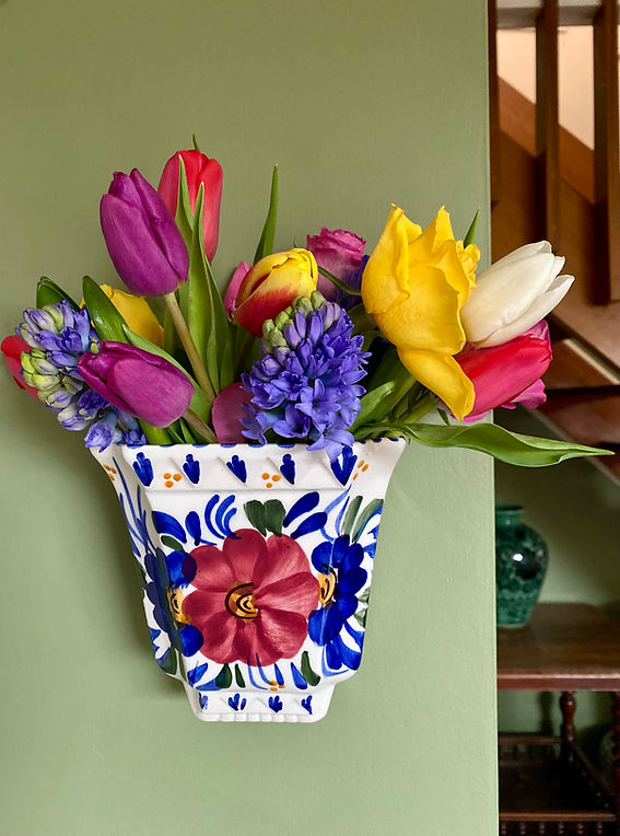 A colourful, hand-painted, wall-mounted flower vase filled with Spring flowers.