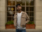 Man in a beige jacket standing outside a warm-toned building