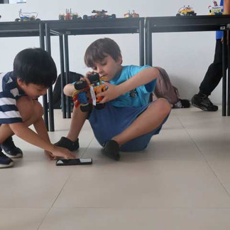 Two students work together on a robotics project, adjusting and testing a robot model on the floor.