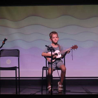 A student plays the ukulele on stage in front of an audience during the showcase presentation.