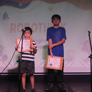 Two students stand on stage holding certificates during the Robotics Club presentation.