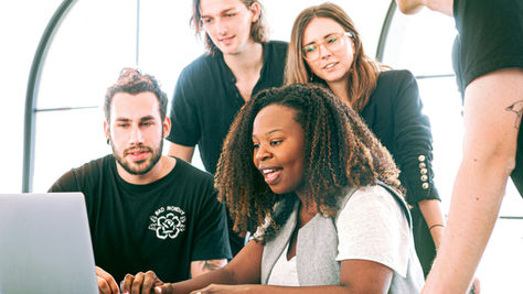 Lady watching her laptop with her team behind her.