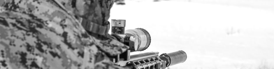 Camouflaged person aiming sniper rifle in snow