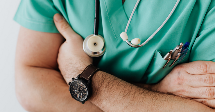 A physician in scrubs with stethoscope crossing his arms