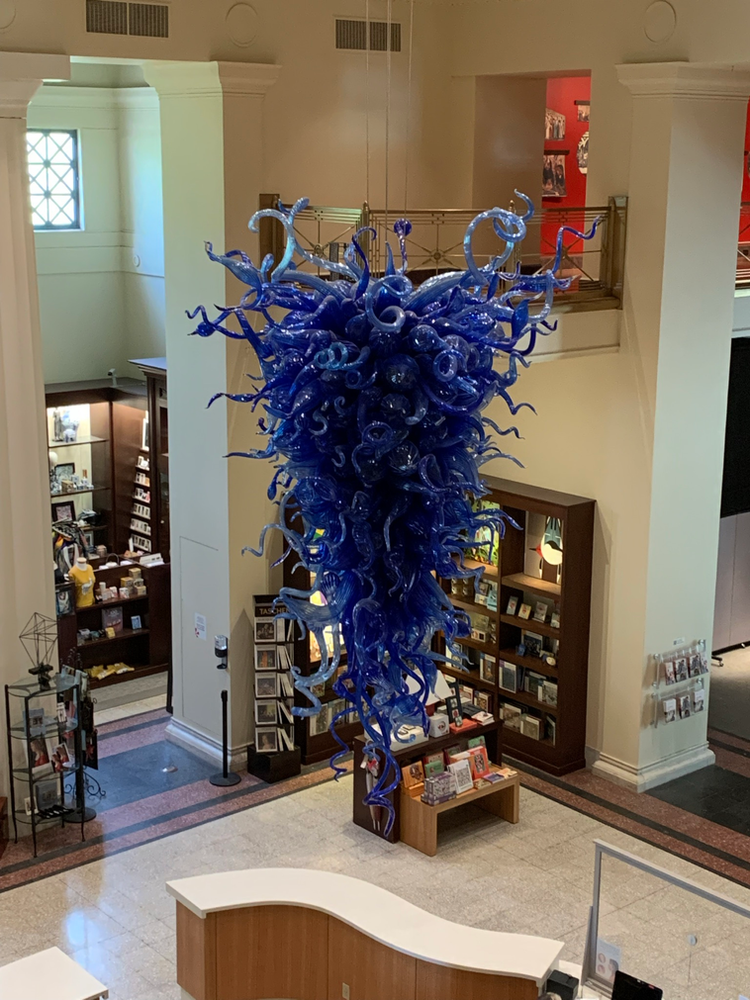 Blue glass sculpture hanging in a museum lobby