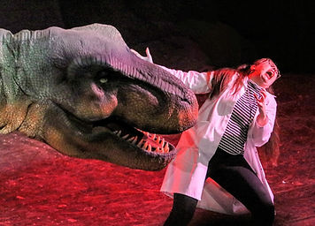 A performer dressed in safari gear interacts with a lifelike triceratops model on stage. Dramatic lighting and a jungle-themed backdrop add to the immersive experience of the dinosaur-themed live show.