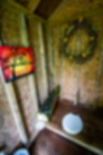 Photo inside primitive toilet with toilet paper inside a mailbox shaped like a fish.