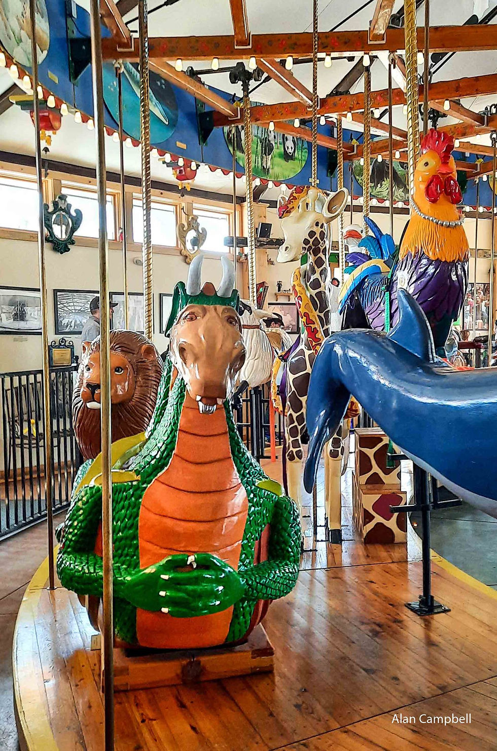 Photo from the carousel looking back at the creatures behind including a dragon, lion giraffe and rooster.