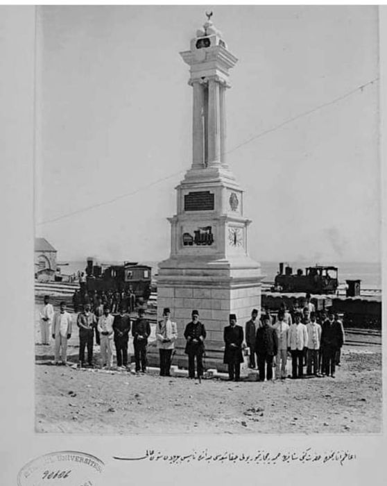 Group of men pose near tall monument and train