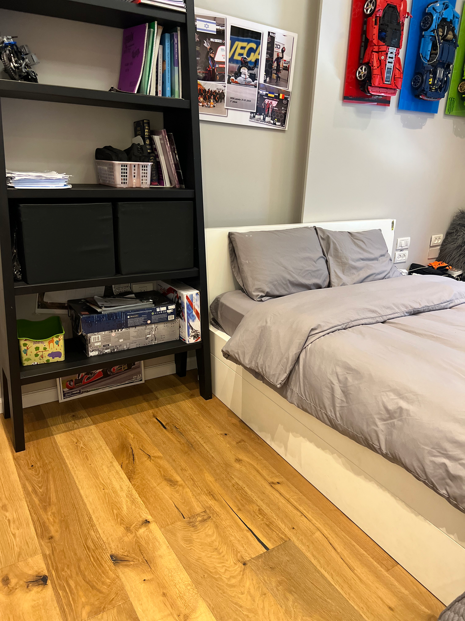 Grey bedding, bookshelf, and wooden floor in bedroom