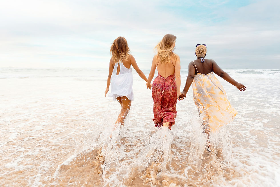 Three women holding hands, walking into the water on the beach.