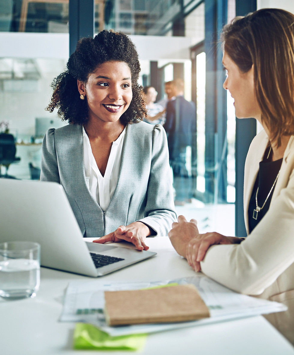 Two women at a desk with a laptop and notes.