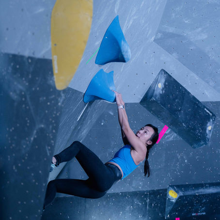 A climber holds on to a climbing hold as they get ready to jump to antoher.
