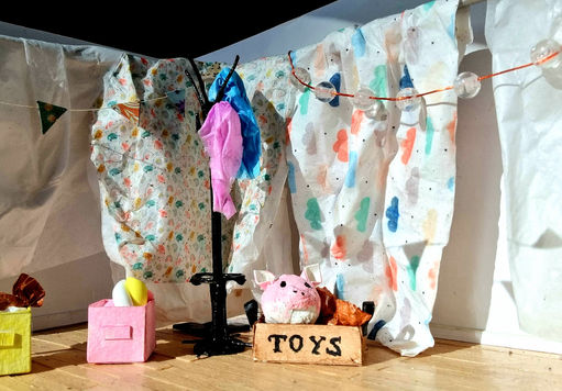 model of coat stand and toy boxes on a wooden floor in front of hanging bed sheet backdrop