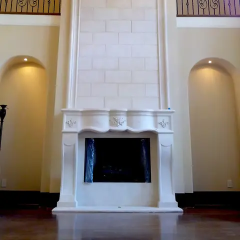 Cream stone fireplace surround with a curvilinear design, framed by soft lighting and decorative archways for a classic look.