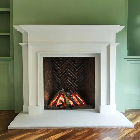 Elegant white fireplace surround set against a green wall, featuring a warm glowing ember display with a herringbone brick.
