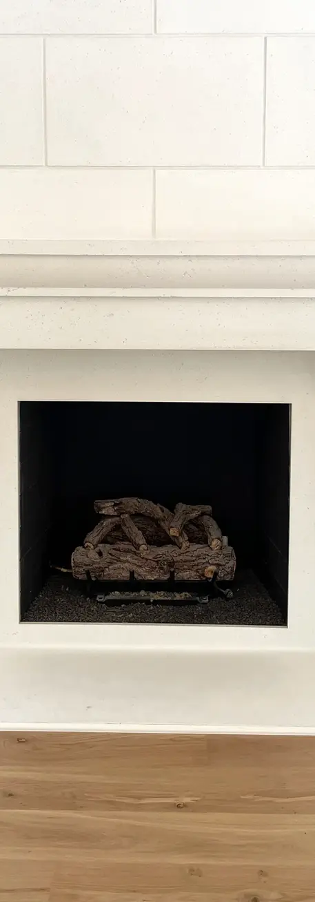 Elegant white fireplace mantel with a modern design, featuring decorative logs and situated against a wood floor backdrop.