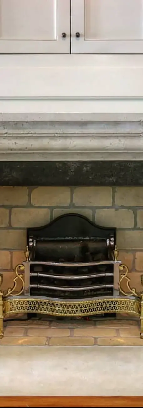 Elegant stone fireplace surround with a decorative brass grate, set against a backdrop of classic brickwork and white cabinet