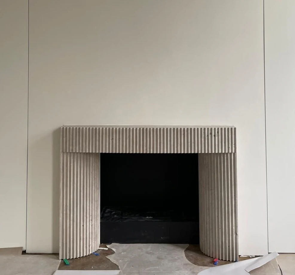 a dark buff fluted stone fireplace surrond wraps around a black firebox opening in this minimalistic construction project