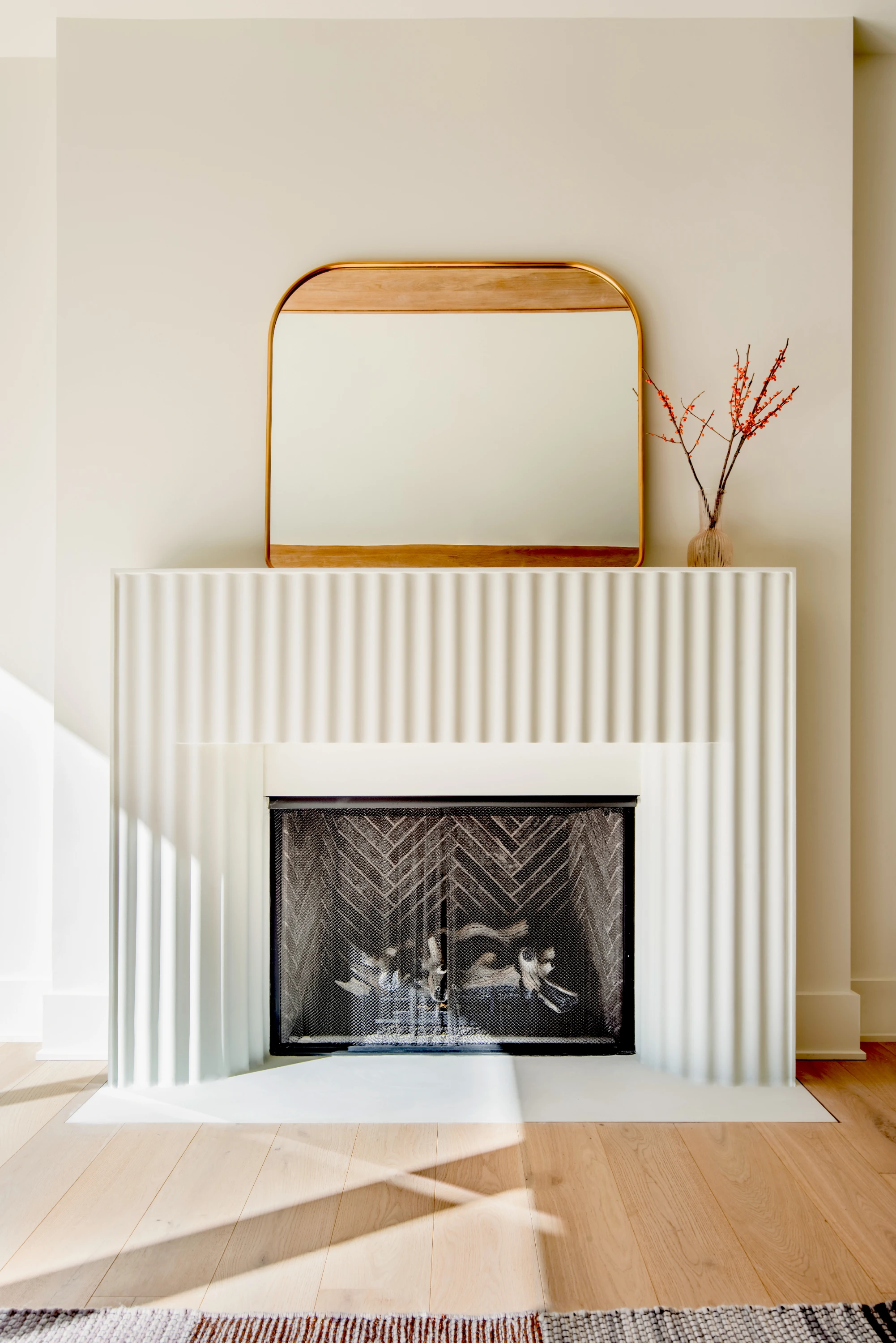 Fluted Stone Fireplace Surround rest beautifully in a well lit interior. It is decorated by an arched mirror and pink blooming twigs.