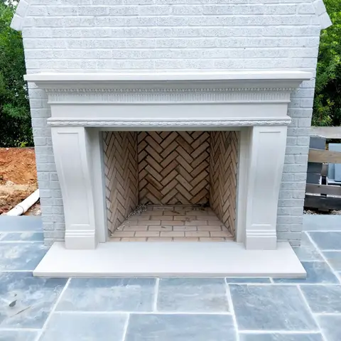 Elegant cast stone fireplace mantel with intricate detailing and a classic herringbone brick interior, set against a textured